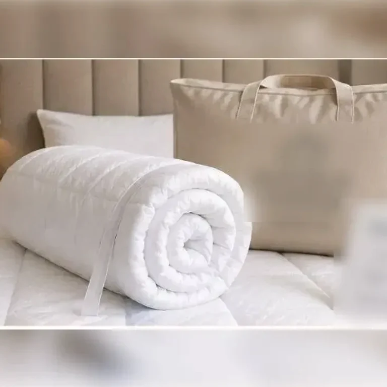 Srolovaný topper v prošívaném potahu a taška na uložení, položené na posteli